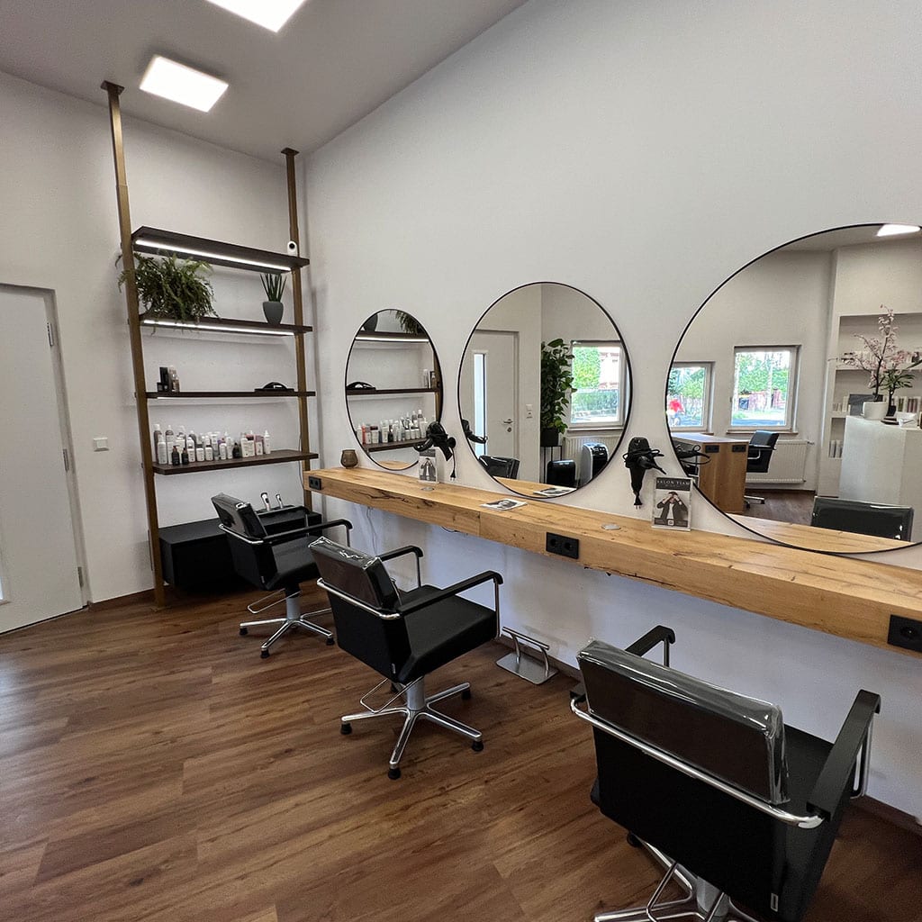 Ein stilvoller Friseursalon mit Holzfußboden, runden Spiegeln und modernen schwarzen Stühlen.